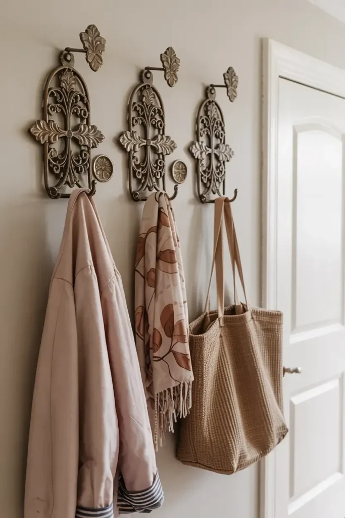 Coat, scarf, and woven bag hanging on decorative metal wall hooks.