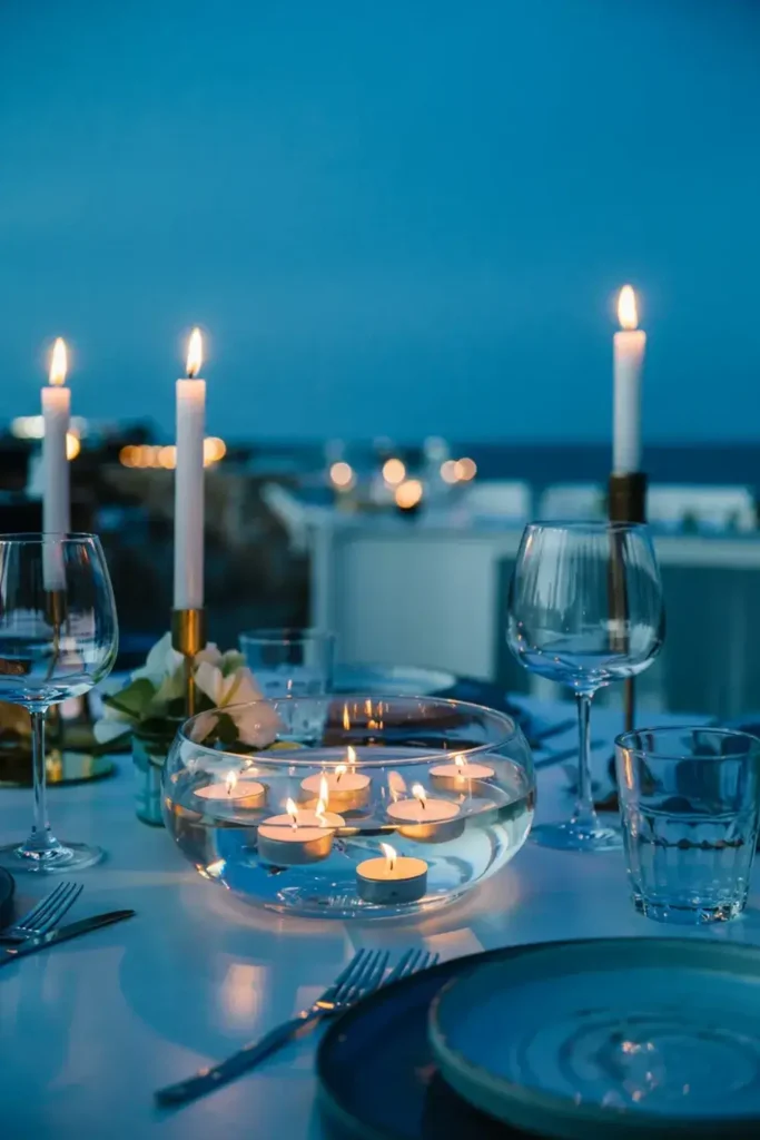 Evening outdoor table setting with lit taper candles and floating tea lights in a bowl.