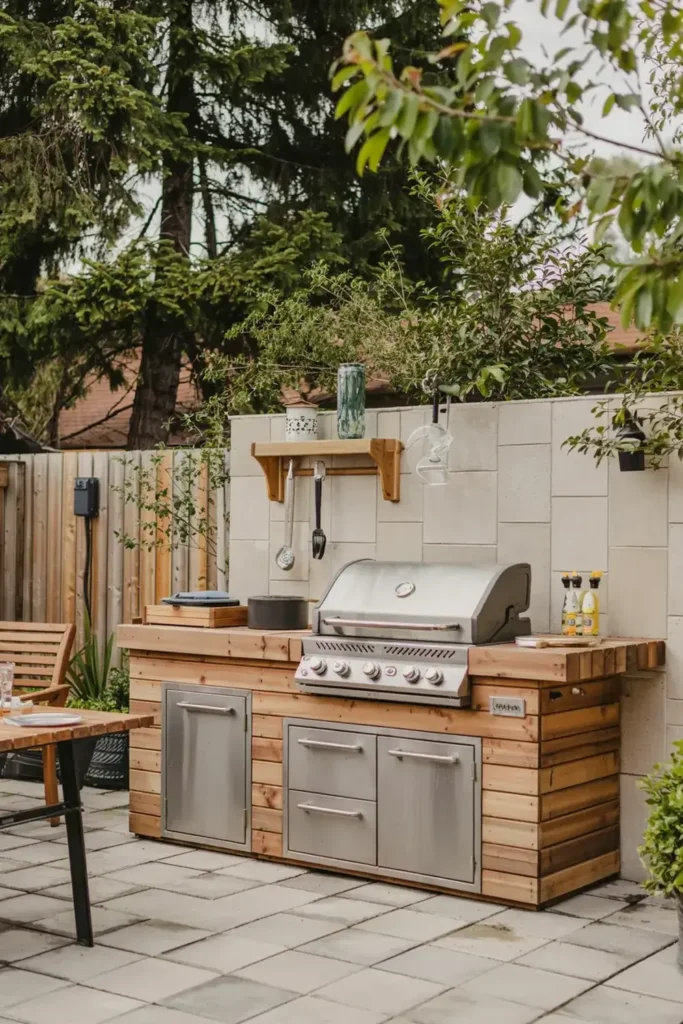 Outdoor kitchen setup with a built-in stainless steel grill and wooden cabinetry on a paved patio.